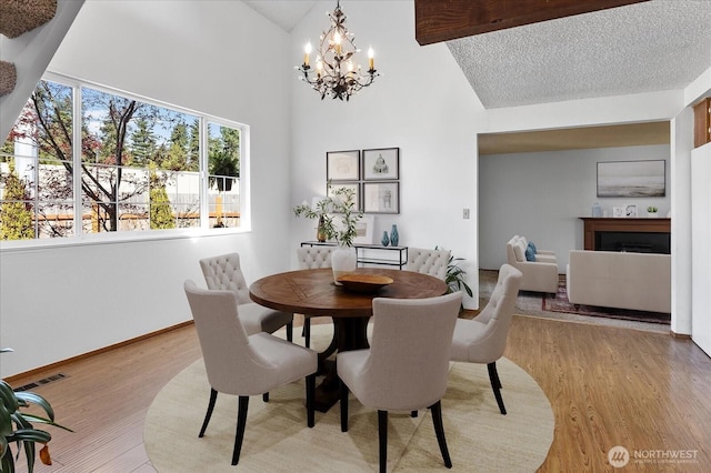 dining space featuring light wood finished floors, visible vents, an inviting chandelier, high vaulted ceiling, and a fireplace