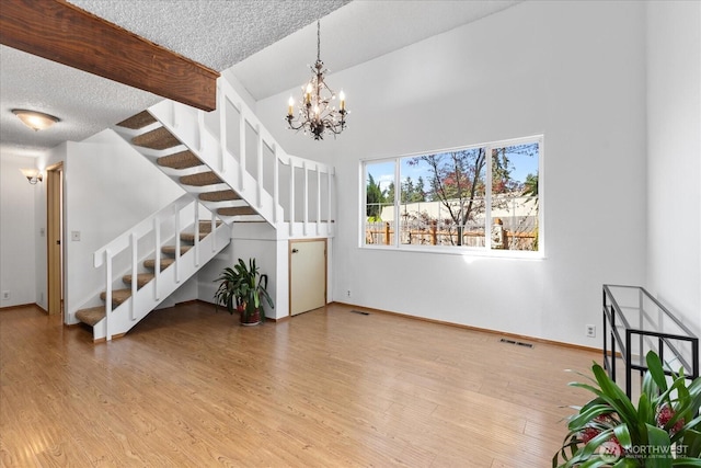 interior space featuring a textured ceiling, visible vents, an inviting chandelier, wood finished floors, and stairs
