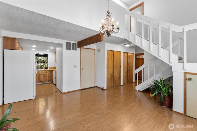 interior space with stairs, a textured ceiling, light wood-style floors, a notable chandelier, and visible vents