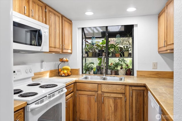 kitchen with light countertops, brown cabinetry, a sink, and white appliances