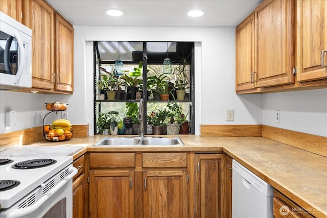 kitchen featuring brown cabinetry, a sink, white appliances, and light countertops