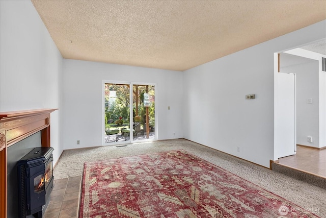 unfurnished living room featuring carpet flooring, a wood stove, a textured ceiling, and visible vents