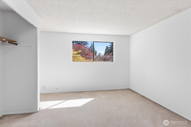spare room with a textured ceiling, carpet flooring, and baseboards