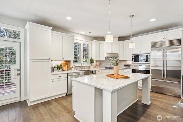 kitchen with a sink, a wealth of natural light, white cabinetry, built in appliances, and wood finished floors