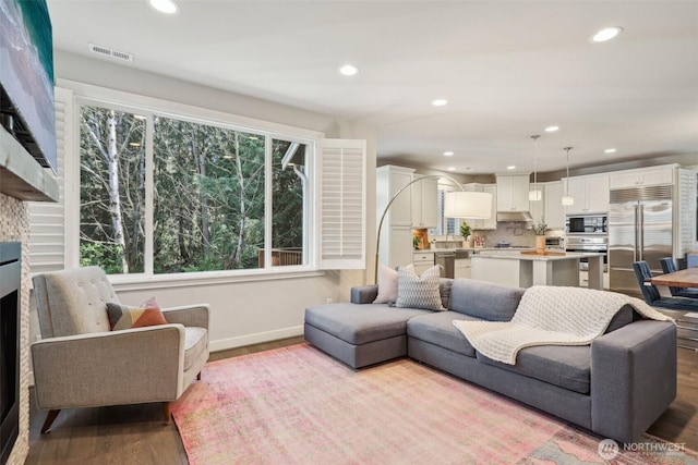 living area with recessed lighting, wood finished floors, visible vents, and baseboards