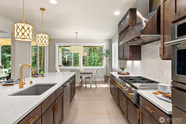 kitchen with a sink, appliances with stainless steel finishes, wall chimney exhaust hood, and dark brown cabinetry