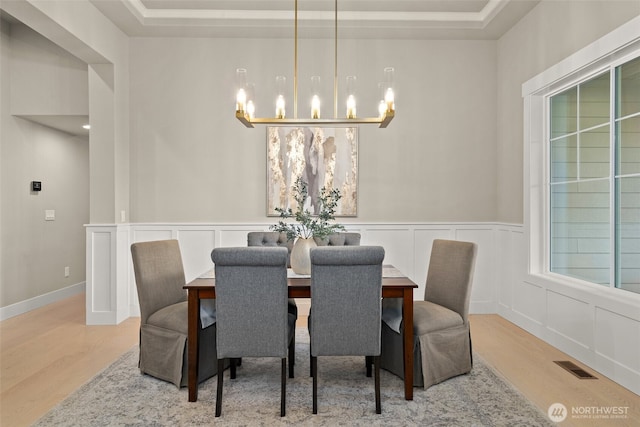 dining room featuring wood finished floors, a tray ceiling, visible vents, a decorative wall, and a chandelier