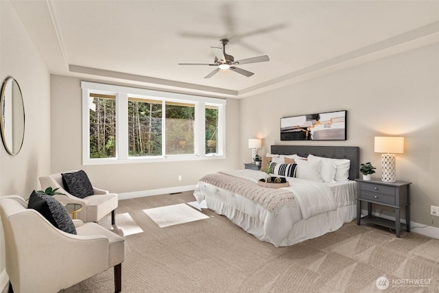 carpeted bedroom with a tray ceiling, baseboards, and a ceiling fan