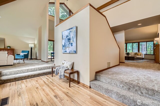 staircase with plenty of natural light, high vaulted ceiling, wood finished floors, and baseboards
