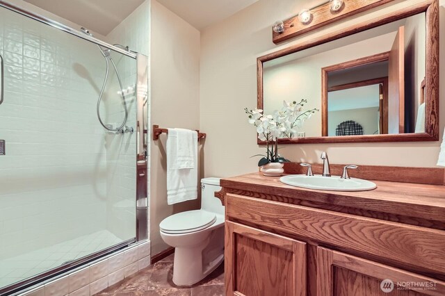 bathroom featuring a stall shower, toilet, vanity, and marble look tiles