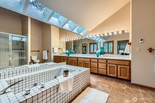 bathroom with a skylight, a stall shower, toilet, double vanity, and baseboards
