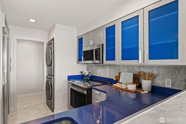 kitchen featuring glass insert cabinets, marble finish floor, stacked washing maching and dryer, dark countertops, and stainless steel appliances
