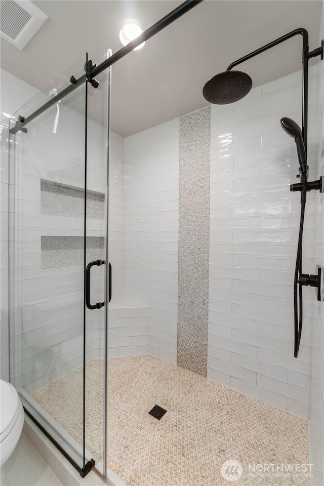 bathroom with a stall shower, toilet, and visible vents