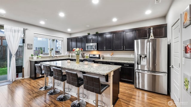 kitchen featuring light wood finished floors, a kitchen breakfast bar, light stone countertops, a kitchen island, and appliances with stainless steel finishes