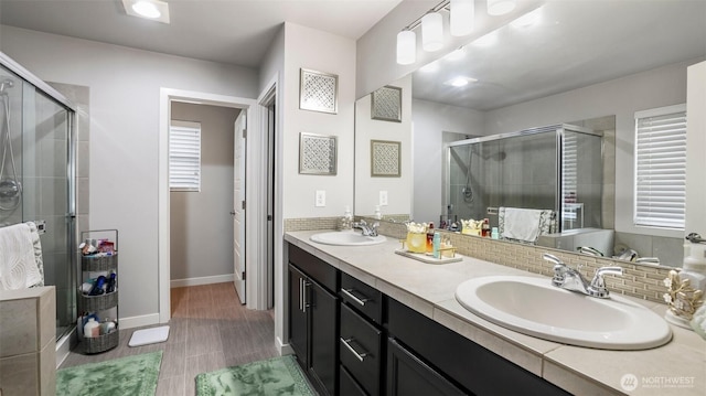 full bathroom featuring baseboards, a sink, double vanity, and a stall shower