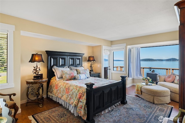 bedroom featuring baseboards, wood finished floors, a water view, and multiple windows