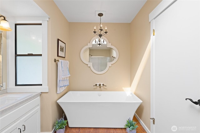 bathroom with a soaking tub, an inviting chandelier, vanity, and wood finished floors