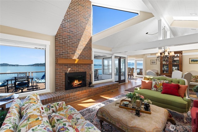 living area featuring a water view, a chandelier, a brick fireplace, wood finished floors, and high vaulted ceiling