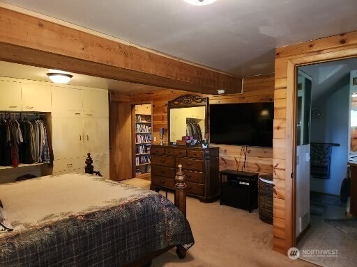 bedroom with wooden walls and light colored carpet