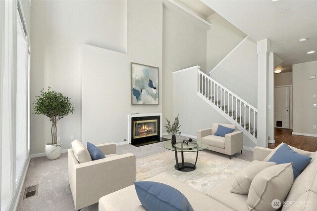 9821 NE Riverbend Dr Unit C102, Bothell, WA 98011 - living room featuring stairway, a glass covered fireplace, a towering ceiling, baseboards, and carpet floors