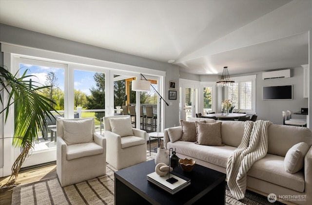 living area with a wall mounted air conditioner, vaulted ceiling, light wood-style floors, french doors, and a notable chandelier