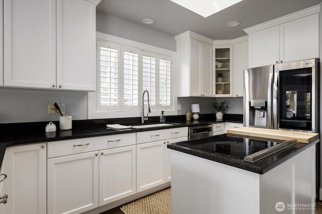 kitchen featuring a center island, a sink, white cabinetry, glass insert cabinets, and appliances with stainless steel finishes