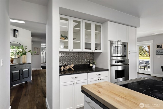 kitchen featuring white cabinets, glass insert cabinets, dark wood-type flooring, and backsplash