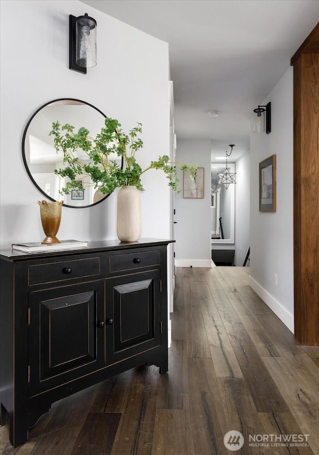 hall featuring dark wood-type flooring, baseboards, and a notable chandelier