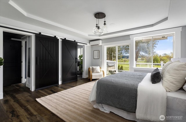 bedroom with a barn door, a wall mounted air conditioner, a tray ceiling, dark wood-type flooring, and access to outside