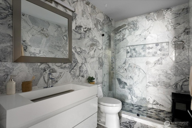 bathroom with tile walls, toilet, vanity, and a marble finish shower