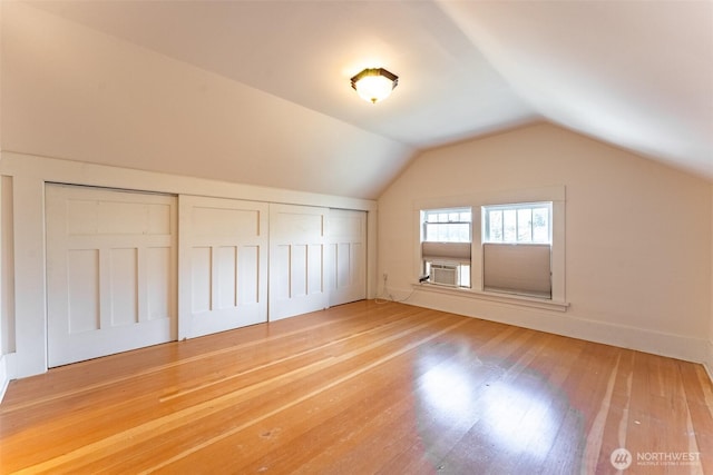 additional living space with cooling unit, vaulted ceiling, and wood finished floors