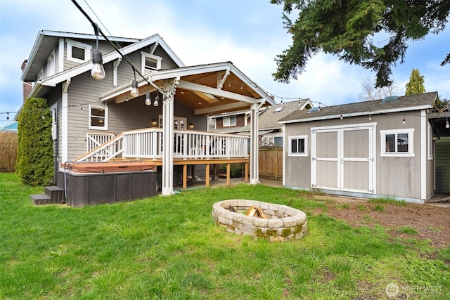 rear view of house with a storage shed, a lawn, an outdoor fire pit, a hot tub, and a wooden deck