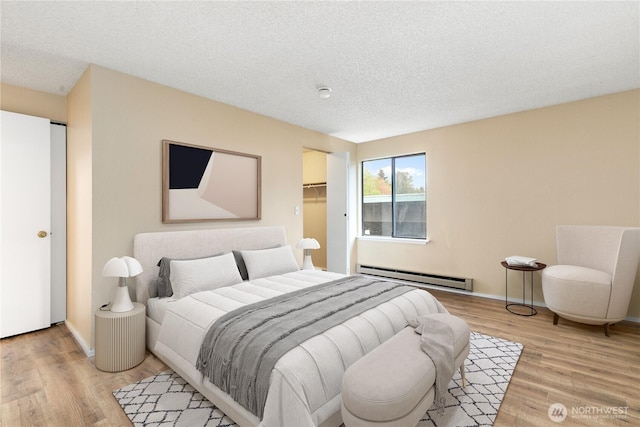 bedroom with baseboards, a baseboard radiator, light wood finished floors, and a textured ceiling