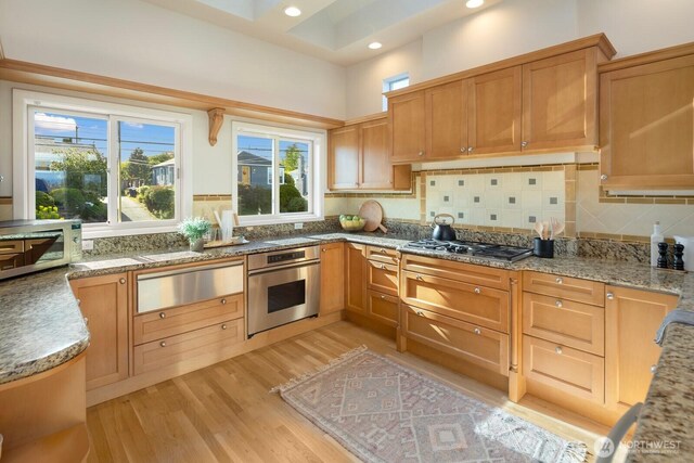 kitchen featuring appliances with stainless steel finishes, a warming drawer, light wood finished floors, light stone counters, and recessed lighting