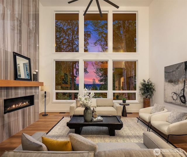 living room with a ceiling fan, wood finished floors, a towering ceiling, a fireplace, and baseboards