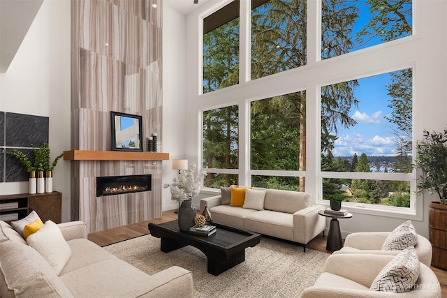 living room with a high ceiling, a glass covered fireplace, and wood finished floors
