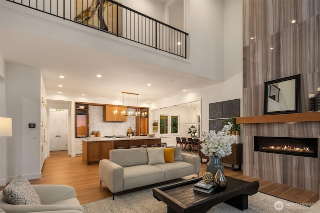 living room featuring light wood-style flooring, a towering ceiling, recessed lighting, a chandelier, and a large fireplace