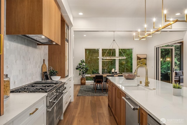 kitchen with dark wood finished floors, stainless steel appliances, wall chimney range hood, a sink, and decorative light fixtures