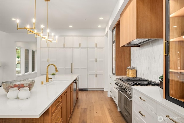 kitchen featuring light wood-style flooring, a sink, white cabinetry, high end range, and premium range hood
