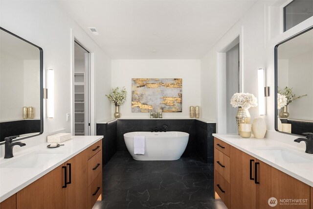 bathroom featuring a soaking tub, marble finish floor, a wainscoted wall, and a sink