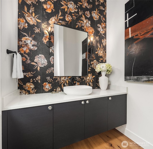 bathroom with wallpapered walls, wood finished floors, vanity, and baseboards