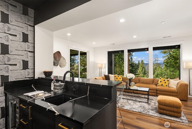 kitchen featuring a sink, open floor plan, recessed lighting, wood finished floors, and dark cabinets