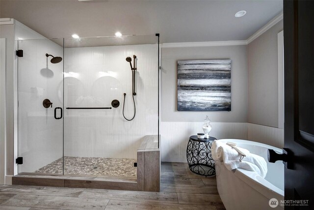 bathroom with a wainscoted wall, a stall shower, wood finished floors, a freestanding tub, and crown molding