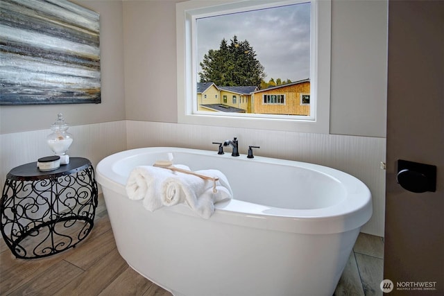 bathroom with wainscoting, a soaking tub, and wood finished floors