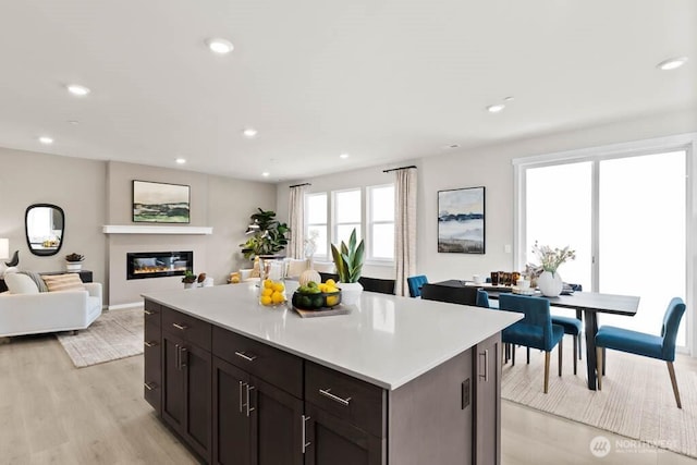 kitchen featuring open floor plan, a glass covered fireplace, light wood-style floors, light countertops, and a kitchen island
