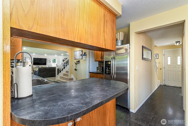 kitchen featuring stainless steel fridge, brown cabinetry, a peninsula, baseboards, and dark countertops