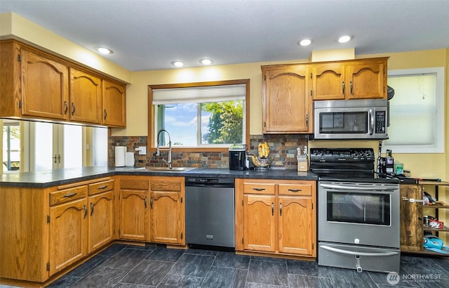 kitchen featuring a sink, stainless steel appliances, brown cabinetry, a peninsula, and dark countertops