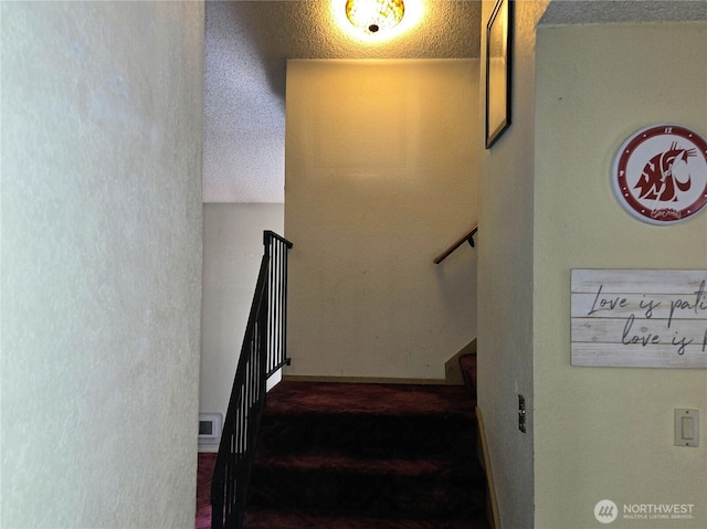 stairway featuring a textured ceiling and carpet floors