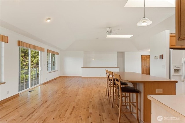 30729 76th Ave NW, Stanwood, WA 98292 - kitchen featuring vaulted ceiling with skylight, light wood-style flooring, a breakfast bar, white fridge with ice dispenser, and light countertops