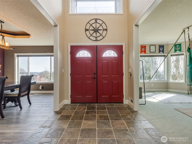 entryway with baseboards, ornamental molding, a textured ceiling, and a wealth of natural light